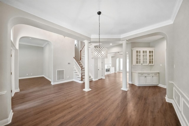 unfurnished dining area featuring dark wood finished floors, visible vents, arched walkways, crown molding, and stairs