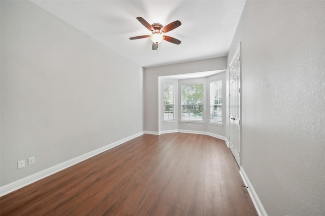 unfurnished room featuring a ceiling fan, baseboards, and dark wood-style flooring