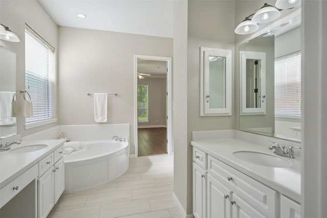 bathroom featuring a garden tub, two vanities, a sink, and baseboards