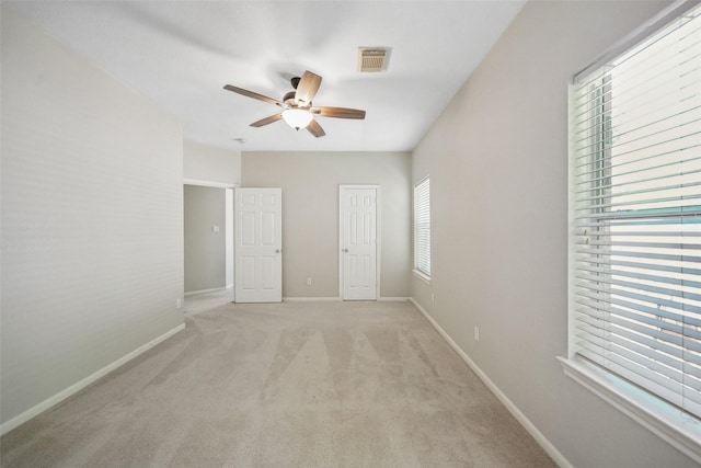 unfurnished bedroom featuring baseboards, visible vents, light colored carpet, and ceiling fan