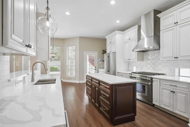 kitchen featuring a sink, recessed lighting, white cabinetry, high end appliances, and wall chimney range hood