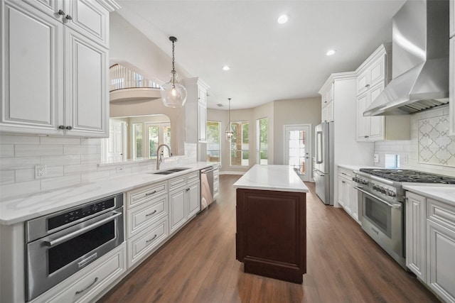 kitchen featuring stainless steel appliances, arched walkways, wall chimney exhaust hood, a center island, and tasteful backsplash