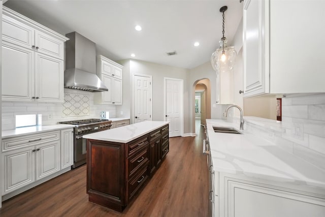 kitchen featuring wall chimney range hood, a sink, arched walkways, white cabinets, and high end stainless steel range oven