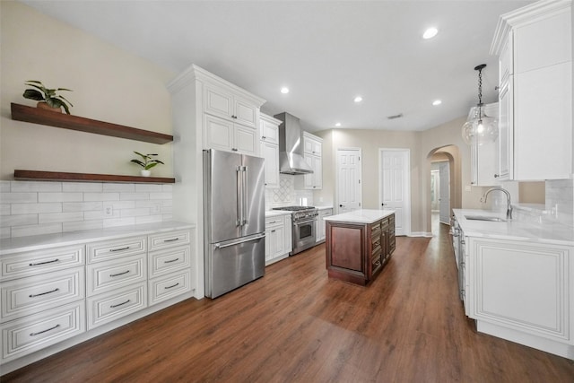 kitchen featuring wall chimney range hood, a sink, arched walkways, a kitchen island, and high quality appliances