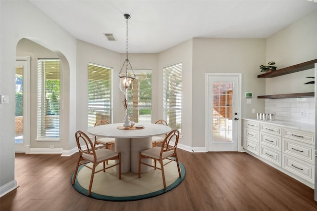 dining space featuring arched walkways, dark wood-type flooring, visible vents, and plenty of natural light