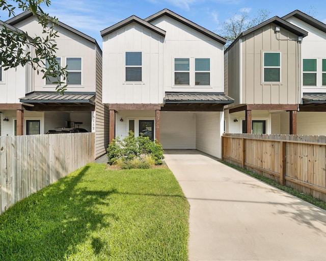 view of property with fence, board and batten siding, a front yard, concrete driveway, and a standing seam roof