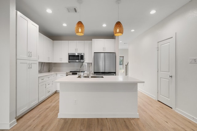 kitchen with visible vents, light wood-style floors, a center island with sink, a sink, and appliances with stainless steel finishes