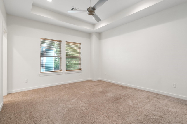 carpeted spare room featuring baseboards, ceiling fan, a tray ceiling, and visible vents