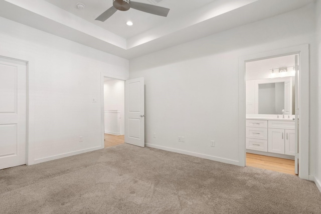 unfurnished bedroom with a sink, baseboards, a raised ceiling, light carpet, and ensuite bath