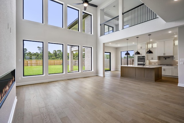 9618 Leafgate Ct, Missouri City, TX 77459 - unfurnished living room with a high ceiling, a ceiling fan, light wood-type flooring, baseboards, and a glass covered fireplace