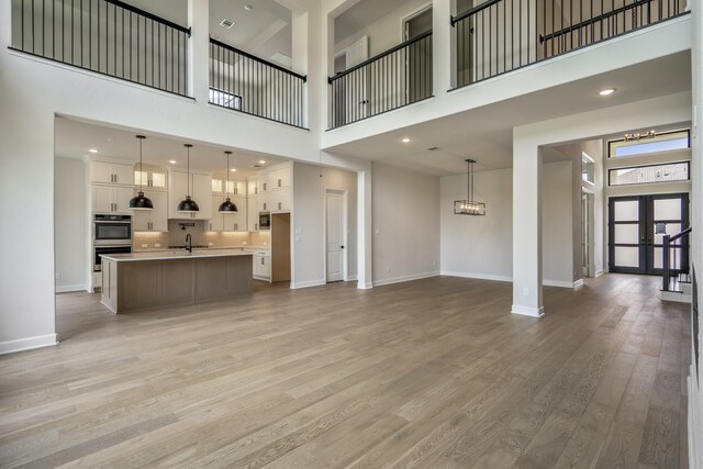 9618 Leafgate Ct, Missouri City, TX 77459 - unfurnished living room featuring a towering ceiling, baseboards, a sink, light wood finished floors, and a chandelier
