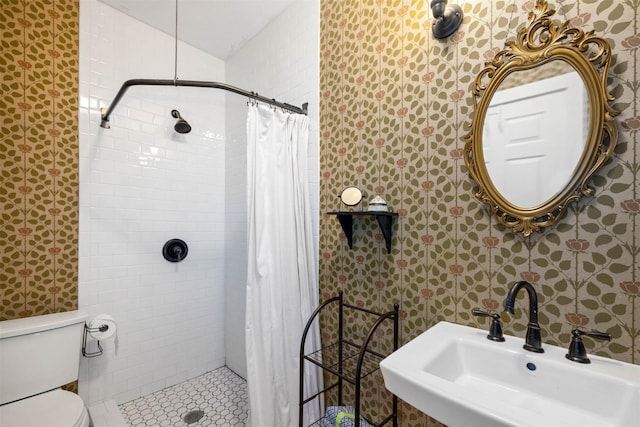 bathroom with toilet, wallpapered walls, a tile shower, and a sink