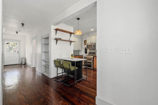 kitchen featuring dark wood-style flooring, appliances with stainless steel finishes, open shelves, baseboards, and a breakfast bar