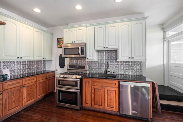 kitchen featuring decorative backsplash, appliances with stainless steel finishes, dark countertops, a sink, and dark wood-style floors