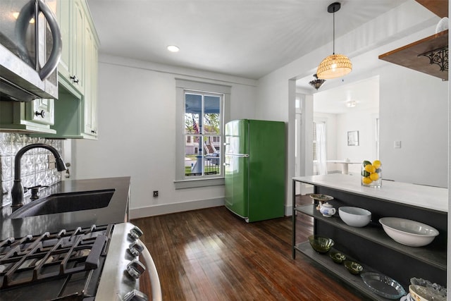 kitchen featuring dark wood-style flooring, appliances with stainless steel finishes, a sink, baseboards, and pendant lighting