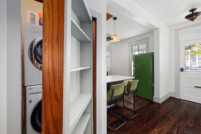 washroom with stacked washer and dryer, laundry area, baseboards, and dark wood-type flooring
