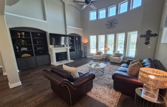 7106 Prairie Grass Ln, Katy, TX 77493 - living room featuring built in shelves, dark wood-style flooring, a ceiling fan, a fireplace with raised hearth, and a high ceiling