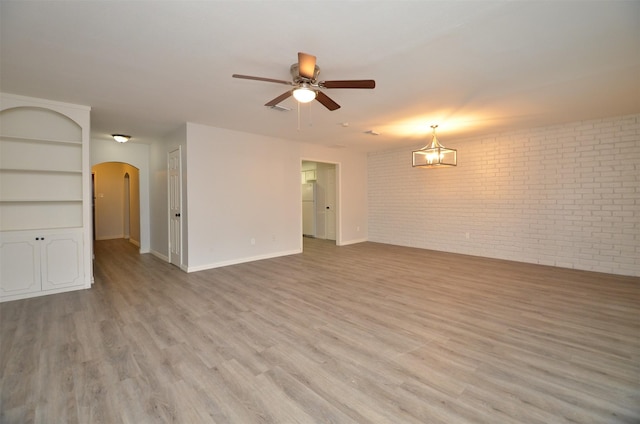 unfurnished room featuring brick wall, arched walkways, light wood-style flooring, and ceiling fan