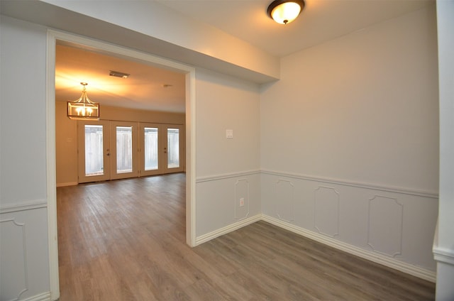 spare room with a decorative wall, visible vents, a chandelier, wood finished floors, and wainscoting