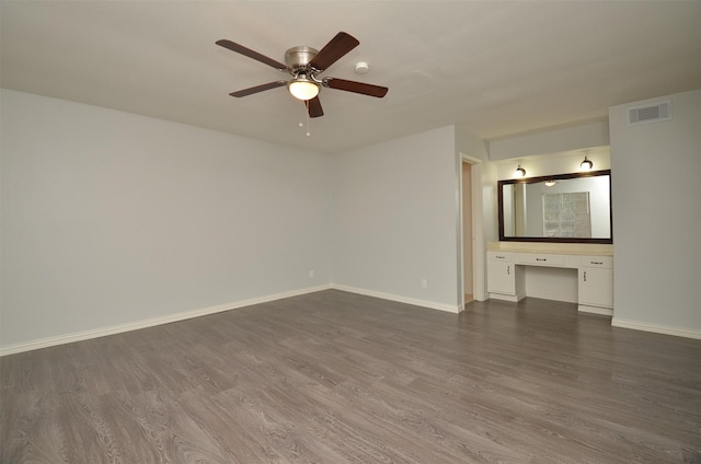 empty room with built in study area, visible vents, ceiling fan, and dark wood finished floors