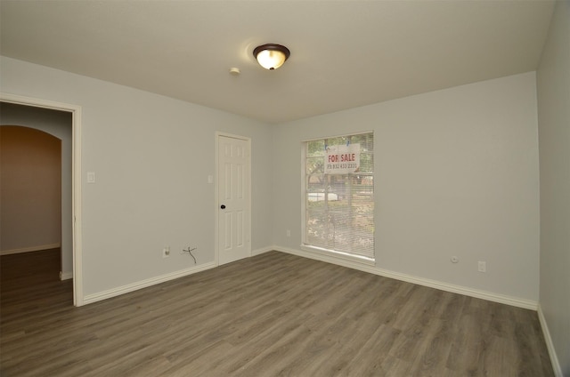 empty room with arched walkways, dark wood-type flooring, and baseboards
