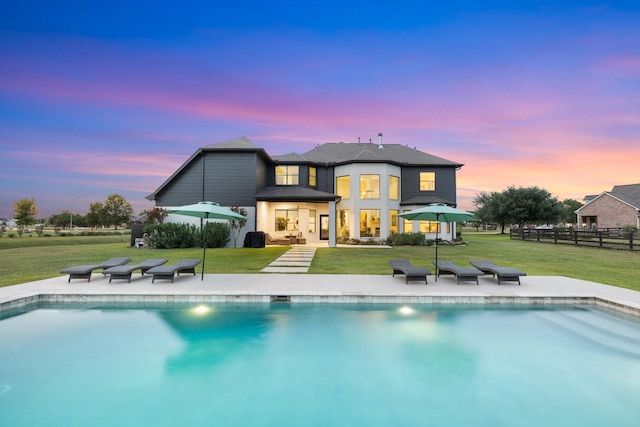 26719 Outback Dr, Katy, TX 77493 - back of house at dusk with an outdoor pool, fence, a patio, and a lawn