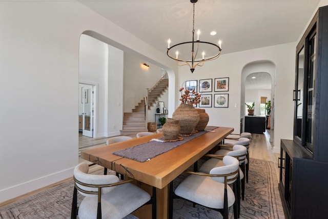 26719 Outback Dr, Katy, TX 77493 - dining space featuring a notable chandelier, light wood-type flooring, baseboards, stairs, and arched walkways