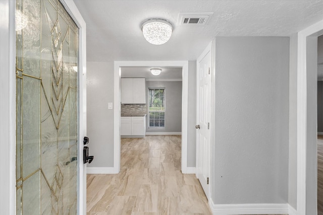 hallway featuring a notable chandelier, a textured ceiling, visible vents, and baseboards