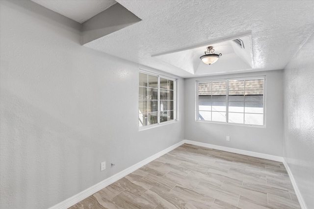 spare room featuring a textured ceiling, a tray ceiling, and baseboards