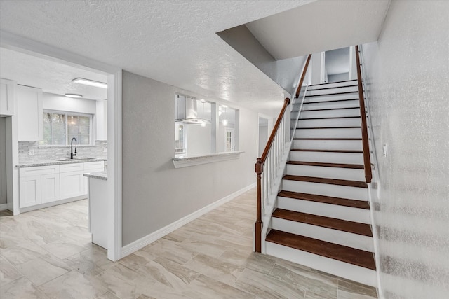 stairway with a textured ceiling, marble finish floor, and baseboards