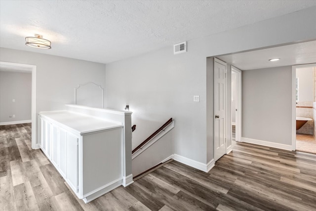 corridor with an upstairs landing, visible vents, wood finished floors, and baseboards