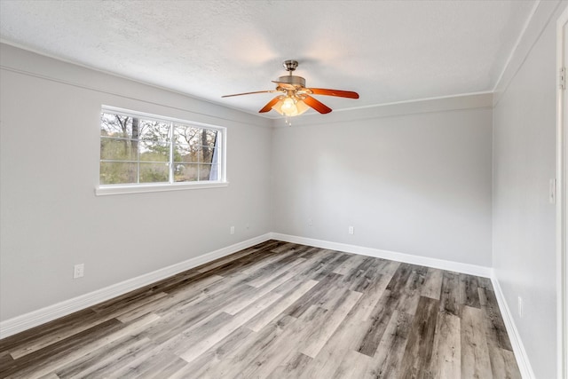 empty room with wood finished floors, ceiling fan, ornamental molding, and baseboards
