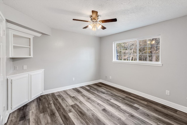 unfurnished room with a textured ceiling, a ceiling fan, dark wood finished floors, and baseboards