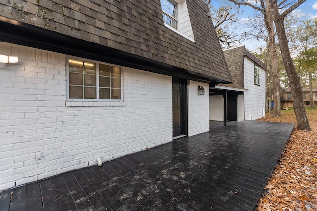 view of property exterior featuring brick siding, a wooden deck, and roof with shingles