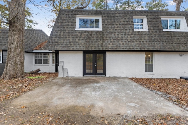 back of house with brick siding, roof with shingles, french doors, and mansard roof