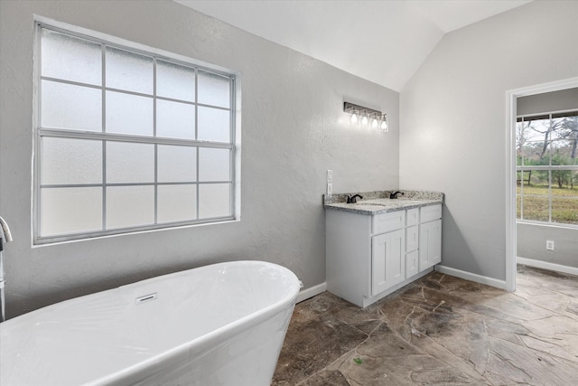 full bath featuring lofted ceiling, a textured wall, vanity, baseboards, and a soaking tub