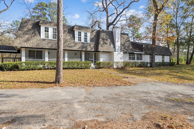 view of front of home featuring a chimney, brick siding, a front yard, and roof with shingles