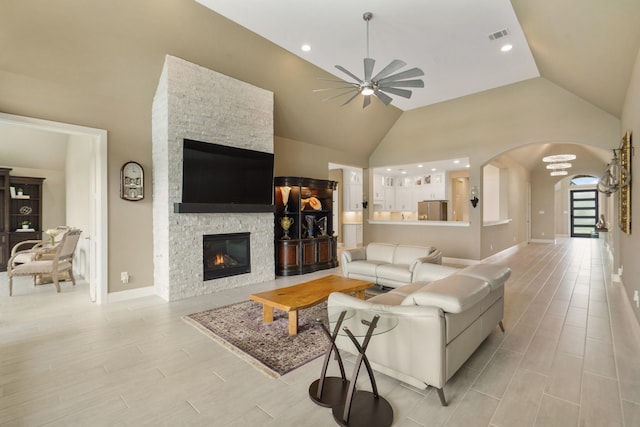 living room with arched walkways, visible vents, light wood-style floors, a ceiling fan, and a stone fireplace