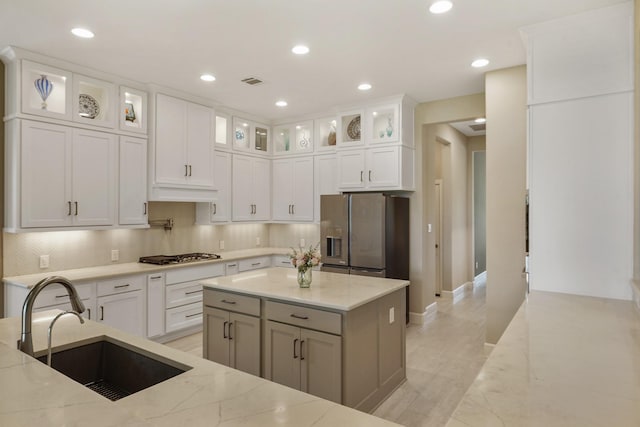 kitchen featuring light stone counters, a sink, white cabinetry, backsplash, and appliances with stainless steel finishes
