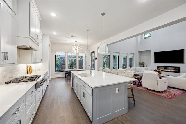 kitchen with a sink, dark wood-style flooring, decorative backsplash, stainless steel gas cooktop, and a breakfast bar area