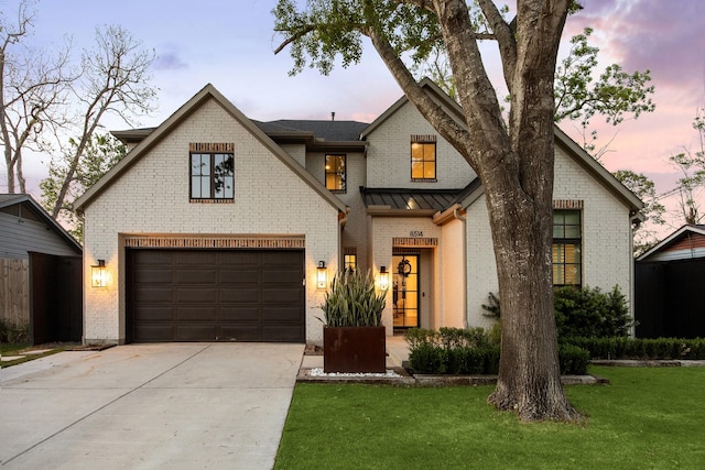 view of front of home featuring driveway, an attached garage, brick siding, a standing seam roof, and a yard