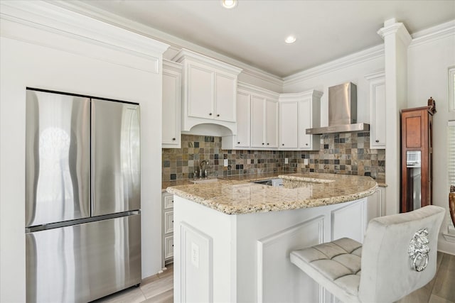 22009 Holly Creek Trl, Tomball, TX 77377 - kitchen with freestanding refrigerator, wall chimney exhaust hood, light stone countertops, white cabinets, and backsplash