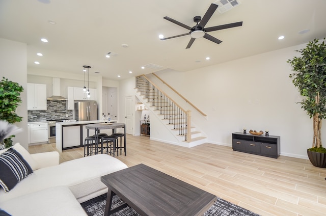 living area featuring stairs, a ceiling fan, recessed lighting, light wood-style flooring, and baseboards
