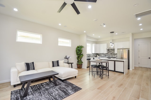 living room featuring a ceiling fan, light wood-style floors, baseboards, and recessed lighting