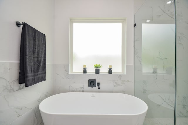 full bath featuring plenty of natural light, a freestanding tub, and tile walls