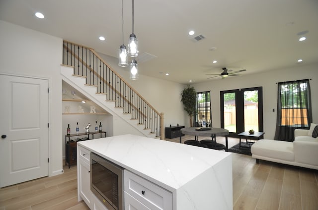 kitchen with stainless steel microwave, open floor plan, light wood finished floors, white cabinetry, and recessed lighting