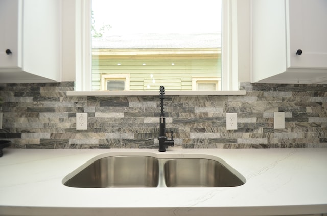 detailed view of a sink, white cabinetry, and backsplash