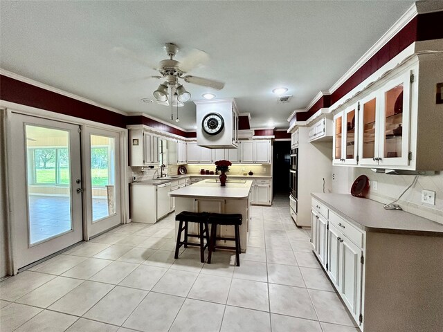 kitchen featuring a ceiling fan, ornamental molding, a kitchen island, light countertops, and a sink