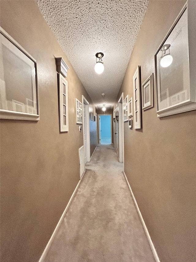 corridor featuring a textured ceiling, baseboards, and carpet