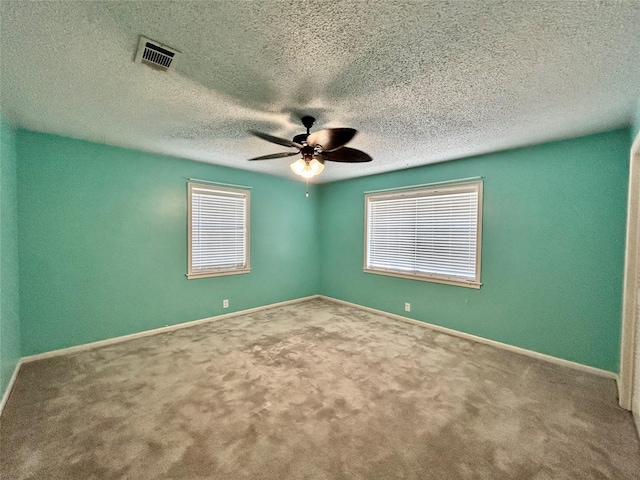 carpeted empty room featuring visible vents, ceiling fan, baseboards, and a textured ceiling